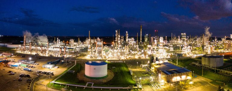 Aerial night view of a brightly lit industrial oil refinery with smoking chimneys in Rosemount, MN, USA.