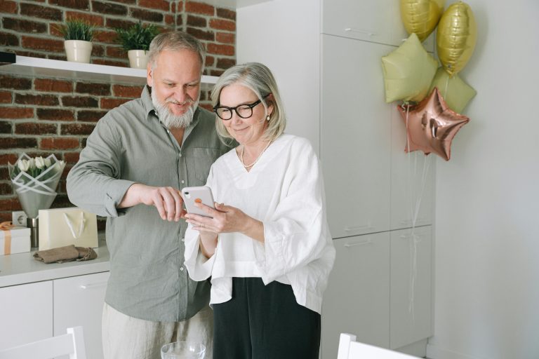 A senior couple enjoying a moment indoors, smiling over a smartphone.
