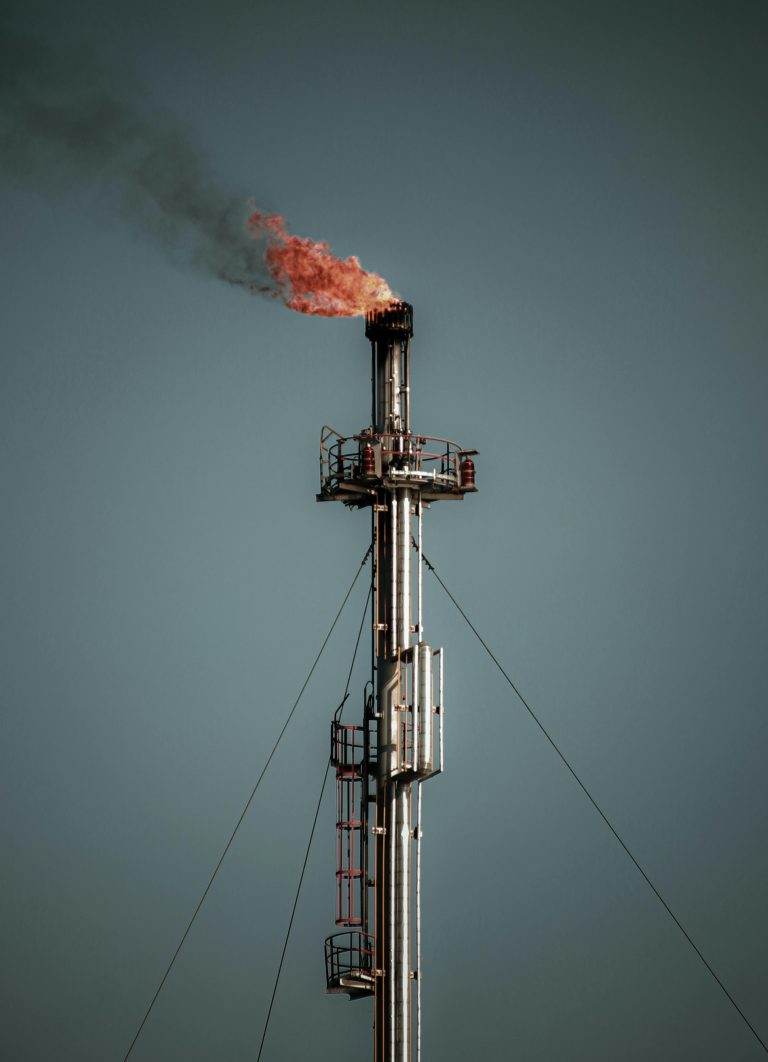 A tall industrial flare stack releasing flame and smoke, set against a clear sky, captures the essence of industrial emissions.